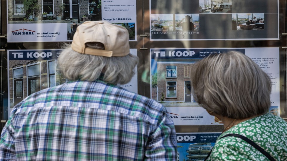 Mensen kijken naar de etalage van een Delftse makelaar.