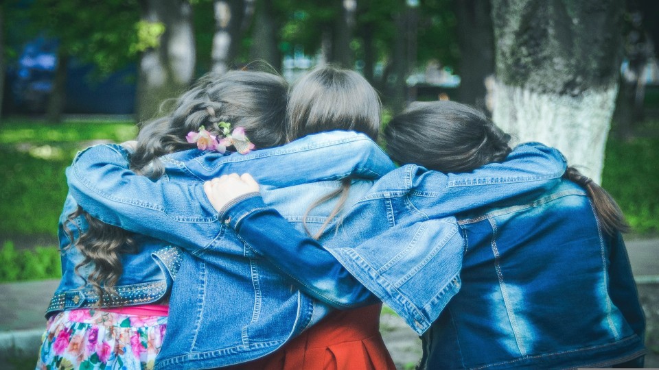 3 meisjes die arm om elkaars schouder slaan, vanaf de rug gezien.
