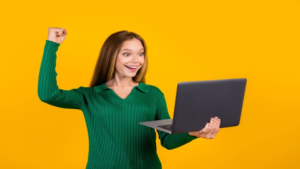 Meisje kijkt blij naar haar laptop, vuist gebald omhoog