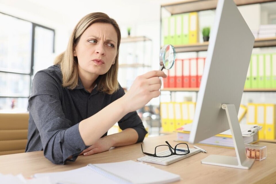 Vrouw kijkt kritisch door loep naar computerscherm