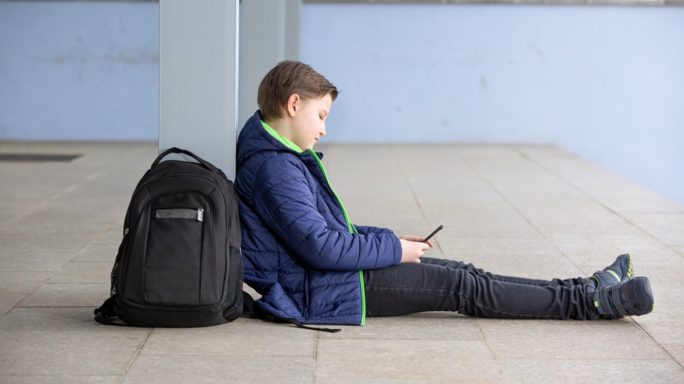 Jong jongetje zit tegen pilaar, kijkt op smartphone