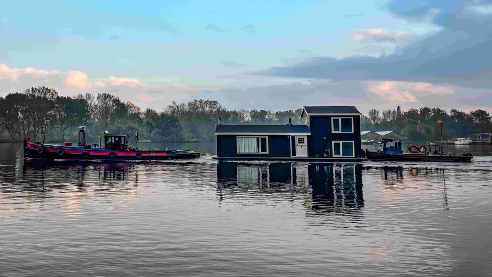Twee sleepboten transporteren een huisje over het water van de Nieuwe Meer in Amsterdam.
