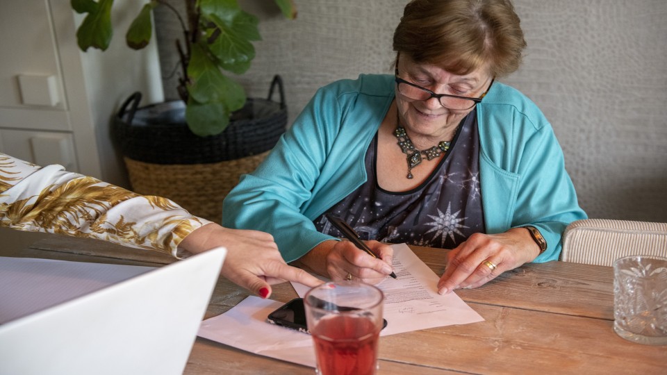 Een dame vult thuis aan de keukentafel formulieren in. Foto: Patricia Rehe/ANP