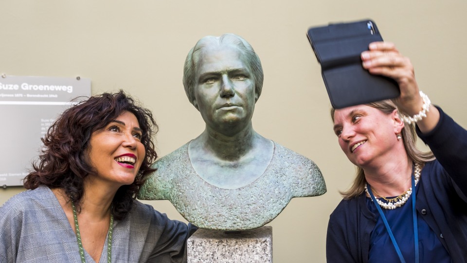 Twee vrouwen maken een foto tijdens de onthulling van het borstbeeld van Suze Groeneweg in de Tweede Kamer.