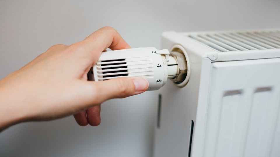 Hand draait aan knop van radiator