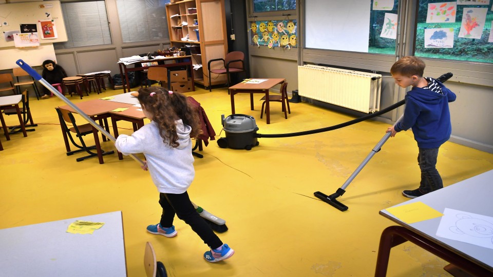 Twee kinderen helpen met het schoonmaken van een klaslokaal. Foto: Marcel van den Bergh (ANP)