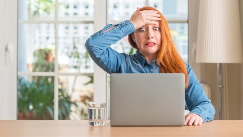 Vrouw achter laptop grijpt ongerust naar voorhoofd