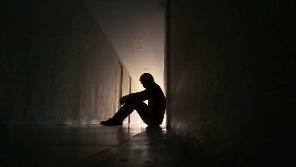 Silhouet van een zittende jongere in een donkere gang met licht op de achtergrond.