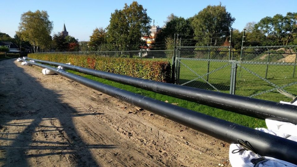Het uitrollen van voorgeïsoleerde verwarmingsbuizen langs een zandweg in Ede
