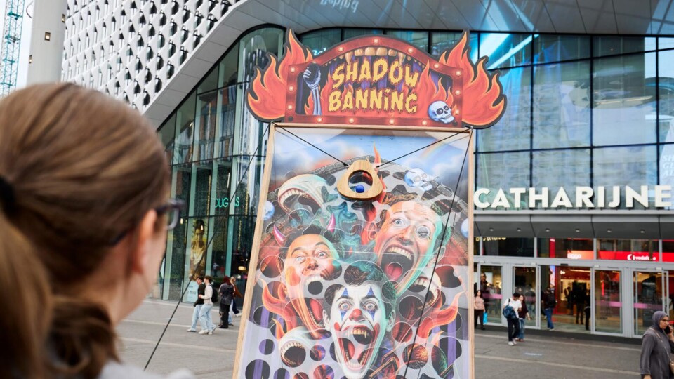 Kunstinstallatie met 'Shadow Banning' bord en kleurrijke gezichten in openbare ruimte voor Hoog Catherijne