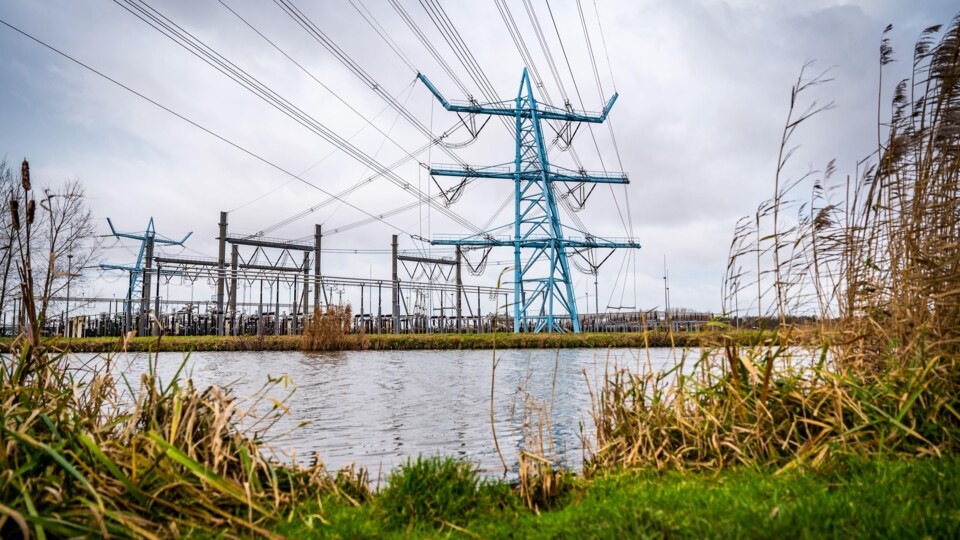 Blauwe elektriciteitsmast en hoogspanningslijnen bij een hoogspanningsstation van Tennet bij water en gras.