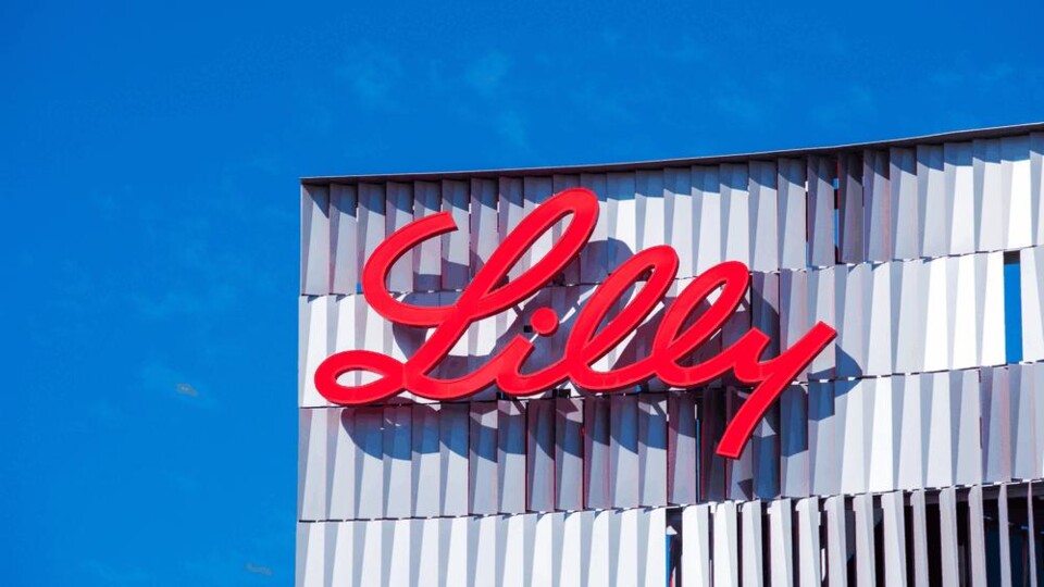 Rood logo met de tekst Lilly op een modern gebouw tegen een blauwe lucht.