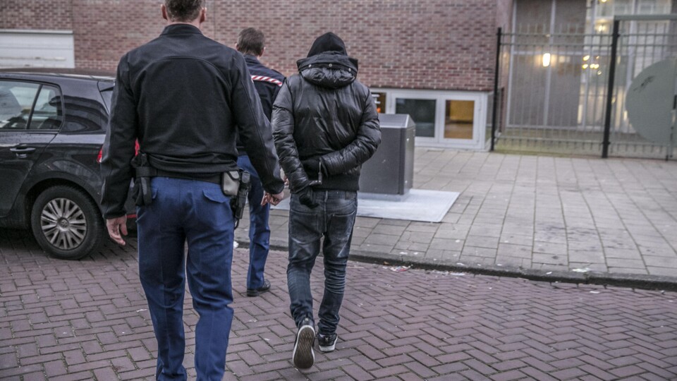 Een jonge verdachte wordt geboeid meegenomen door twee politieagenten