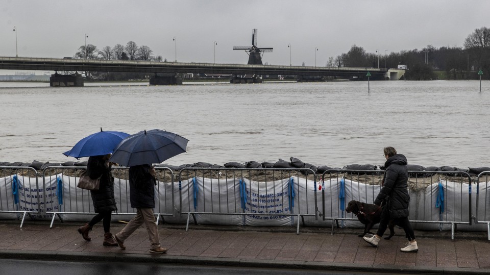 Mensen kijken naar het hoge water in de IJssel bij geplaatste zandzakken in Deventer.