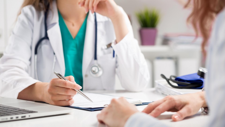 vrouw in witte doktersjas tegenover vrouw, gezichten niet zichtbaar