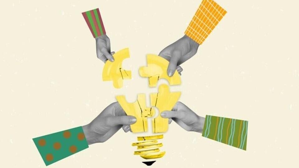 Vier handen met gekleurde mouwen houden gele puzzelstukjes die samen een gloeilamp vormen tegen een lichte achtergrond.