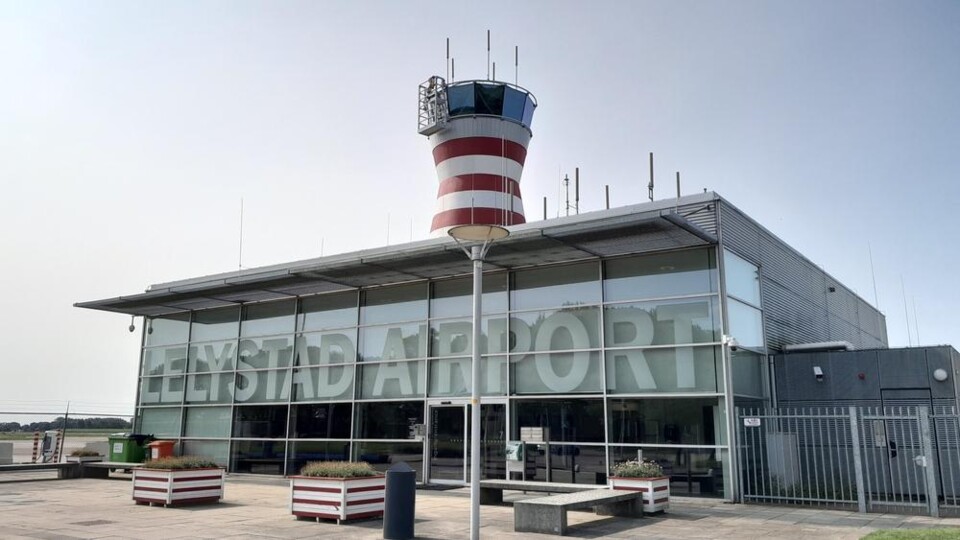 Lelystad Airport gebouw met glazen gevel en rode-witte verkeerstoren op een heldere dag