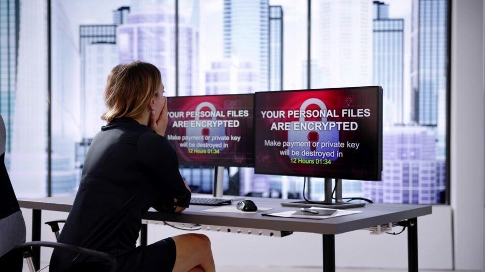 Vrouw staart met hand voor mond naar computerschermen met de tekst 'Your personal files are encrypted'