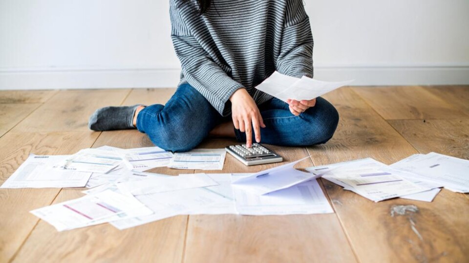 Persoon zit op vloer met rekenmachine, omringd door financiële documenten en rekeningen.