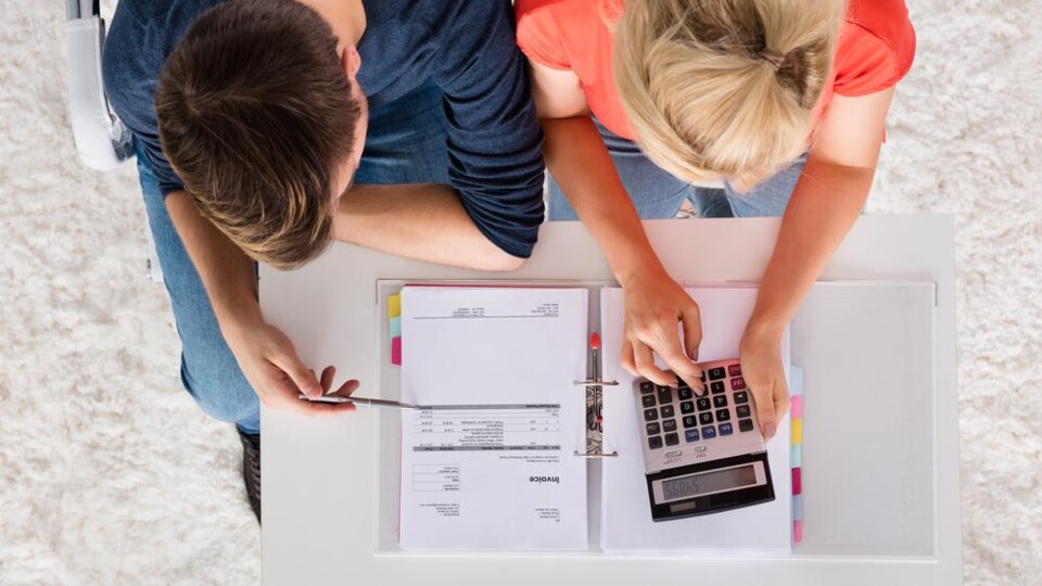 Bovenaanzicht van twee personen die schuldregelingsdocumenten en calculator bekijken