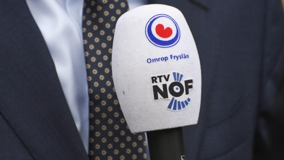 Witte microfoonkop met logo's van Omrop Fryslân en RTV NOF, voor een man in donker pak.