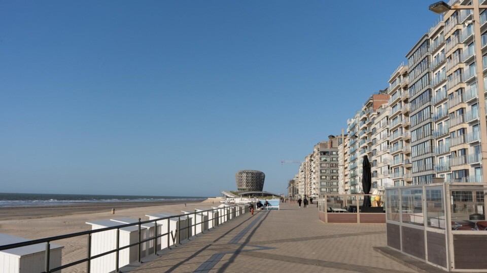 Boulevard met mensen, rij hoge appartementen en strand aan de Belgische kust in Middelkerke bij helder weer.
