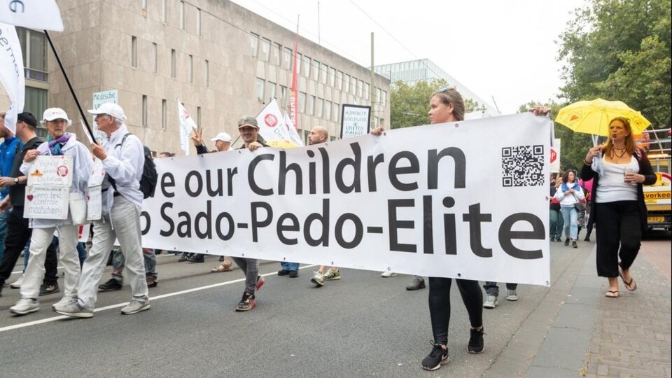 Demonstranten in coronatijd met een spandoek: Save our Children from Sado-Pedo-Elite