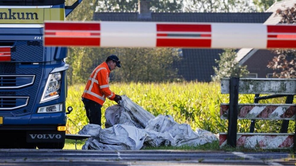 Man in oranje hesje doet iets met witte vuilniszakken naast het spoor
