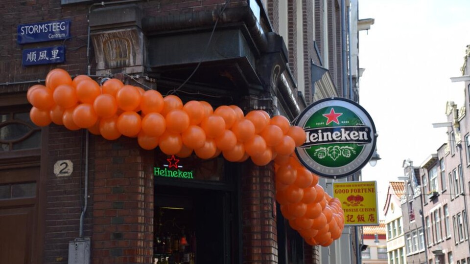 Voorgevel van een horecazaak met oranje ballonnen en Heineken-bord in een Nederlandse straat tijdens het WK voetbal.