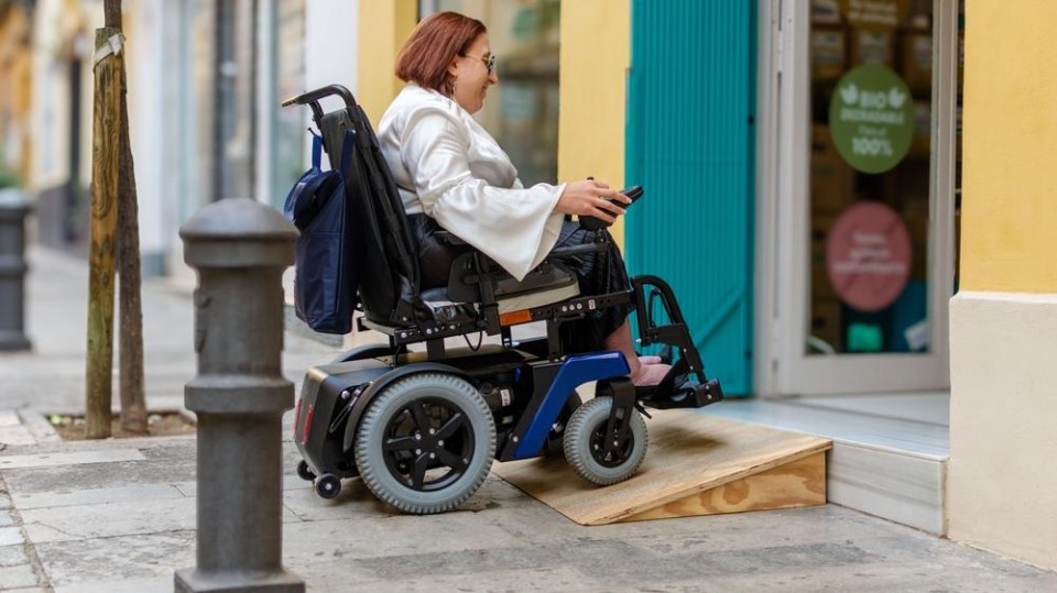 Vrouw in rolstoel rijdt over drempel winkel binnen
