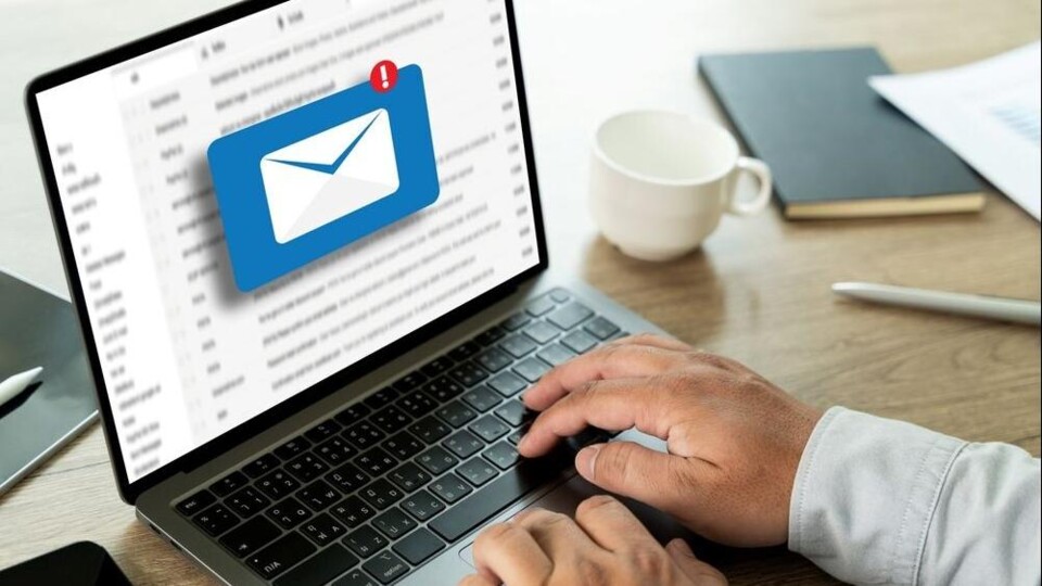 Handen typen op laptop met scherm waarop een e-mail inbox en een pop-up van een nieuw e-mailbericht te zien zijn.