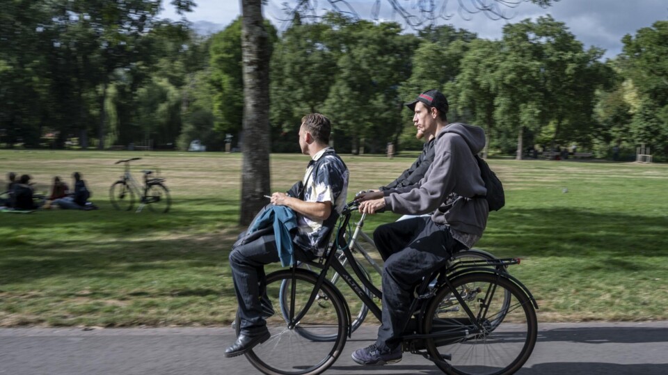 Twee jonge mannen fietsen samen door een groen park met bomen en gras in Amsterdam.