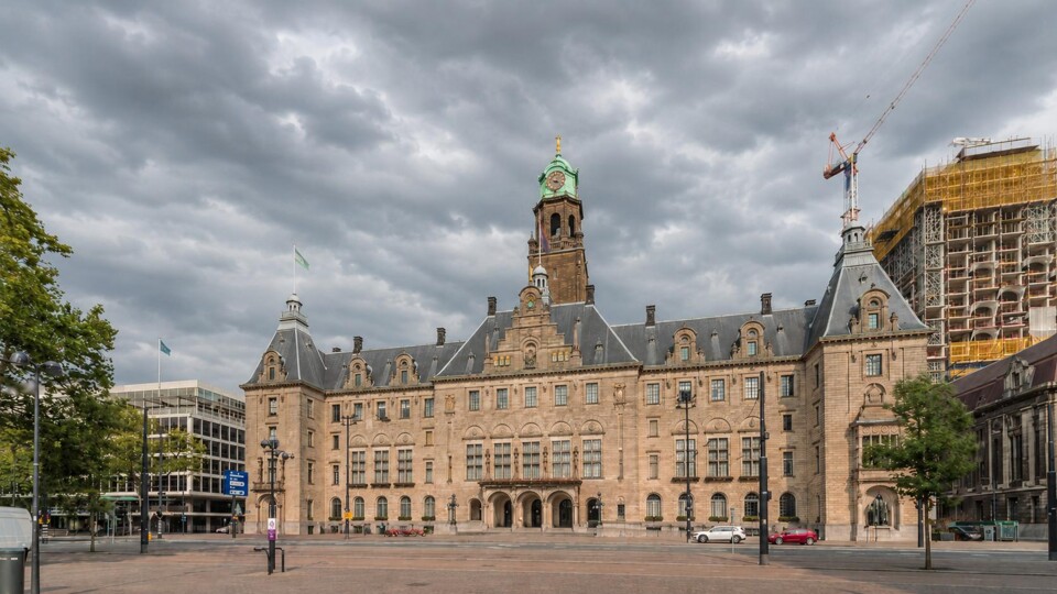 Het stadhuis van Rotterdam met kloktoren, omliggende gebouwen en een bewolkte lucht.