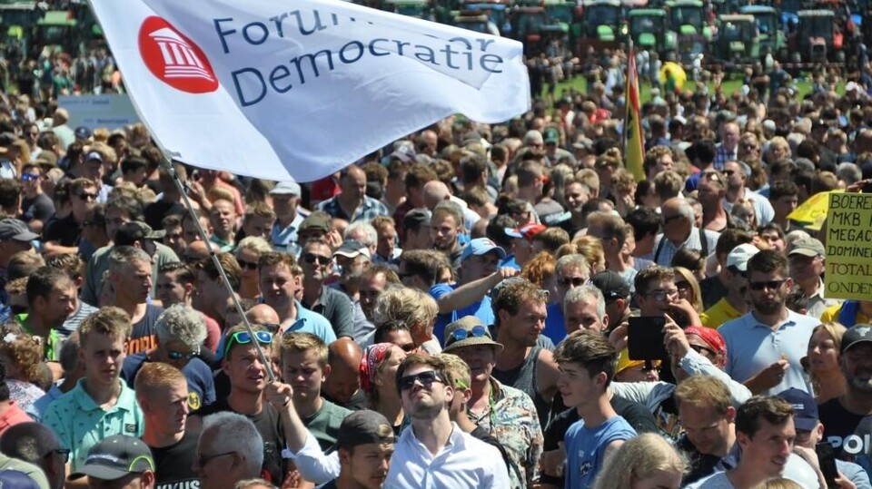 Grote menigte mensen bij demonstratie met Forum voor Democratie vlag in de lucht.
