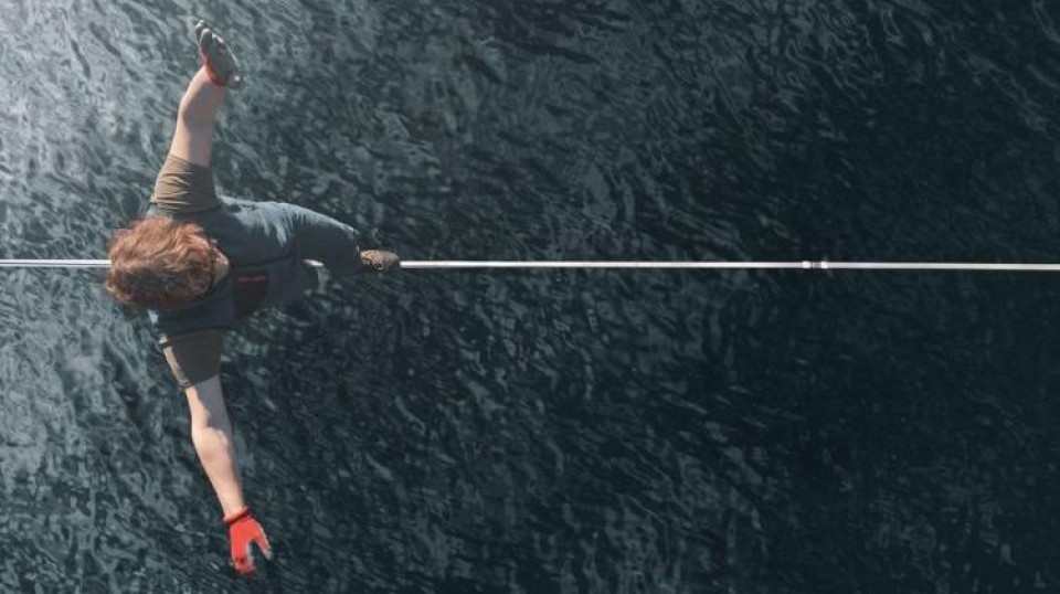 Een man balanceert op een koord over het water, van bovenaf gezien