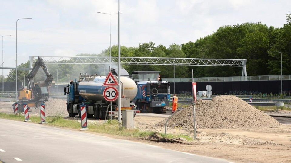 Wegenbouwplaats met graafmachine, tankwagen en bouwmaterialen
