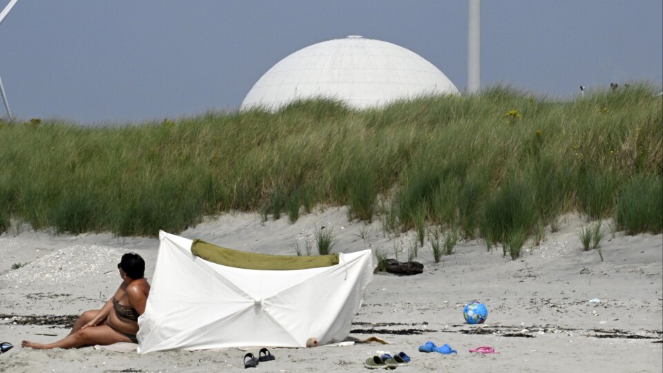 Strand met zand, een persoon zittend naast een witte parasol, op de achtergrond grasduinen en de witte koepel van kerncentrale Borssele.