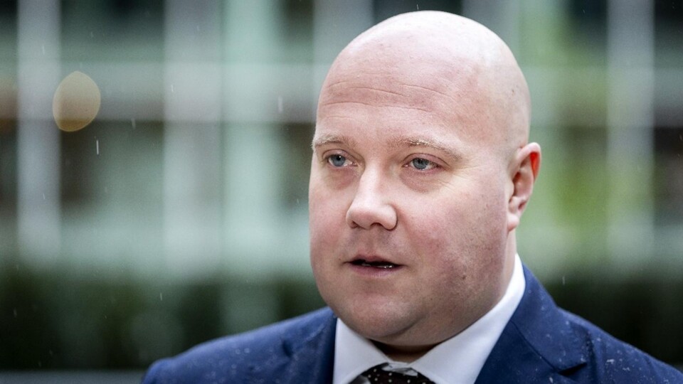 Portret van een kale man in een donkerblauw pak en stropdas, staand buiten bij regenachtig weer.