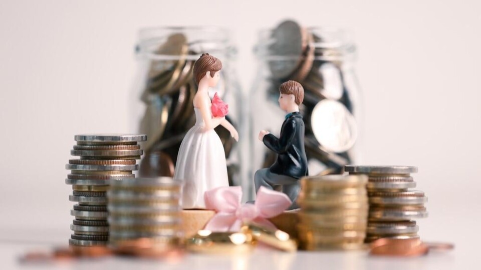 Miniatuurfiguren van een bruid en bruidegom tussen stapels munten en glazen potten gevuld met munten.