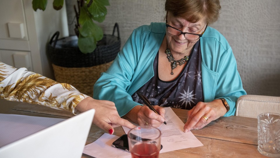 Een vrouw vult thuis aan de keukentafel formulieren in