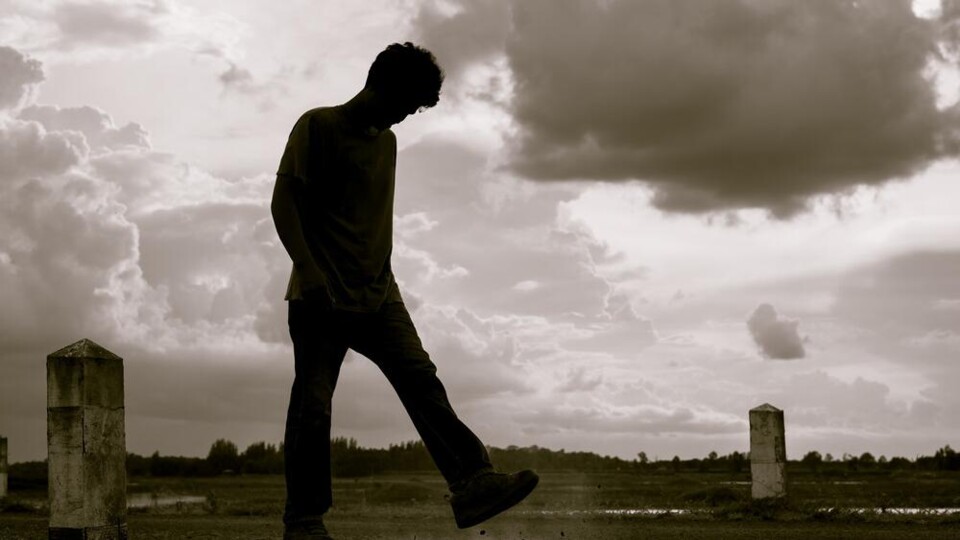 Silhouet van een jonge man die op een open veld staat met bewolkte lucht op de achtergrond.