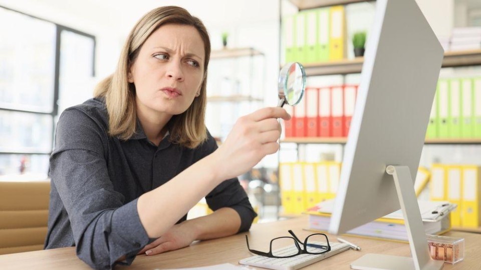 Vrouw kijkt met vergrootglas naar computerscherm