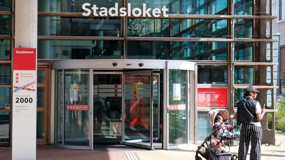 Ingang van het stadsloket Amsterdam met een vrouw die een kinderwagen duwt voor de deur.
