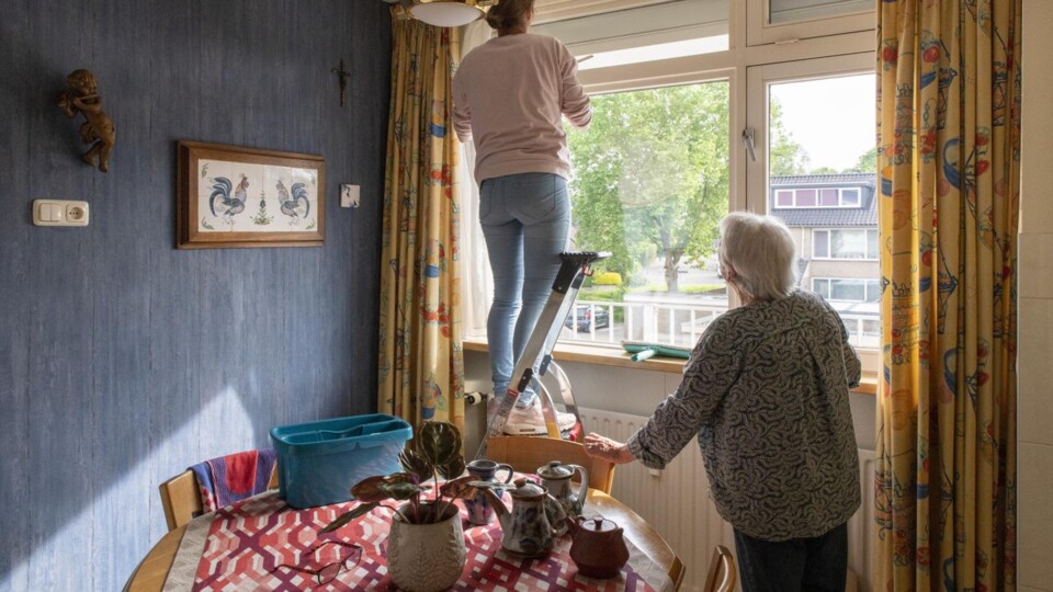 Een vrouw lapt de ramen van een andere, oudere vrouw