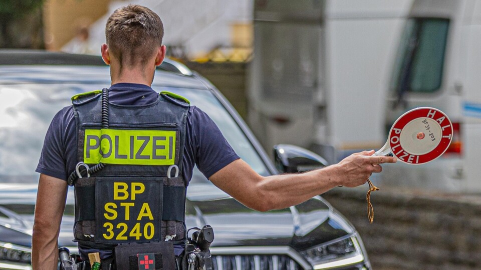 Duitse politieagent met POLIZEI-vest houdt een stopbord vast bij een auto tijdens grenscontrole.
