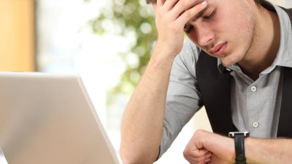 Man achter laptop kijkt op horloge