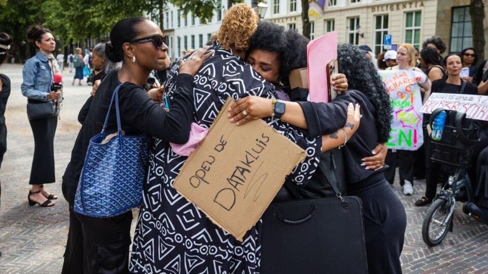 Een groep vrouwen, in het zwart gekleed, omhelst elkaar. Eén van hen draagt een kartonnen protestbord met de tekst 'Open de datakluis'. 